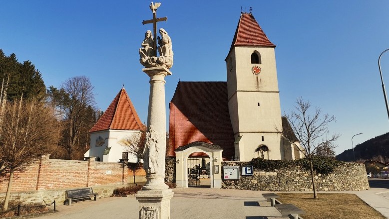 Parish church Unter-Aspang with column in the foreground and blue sky.