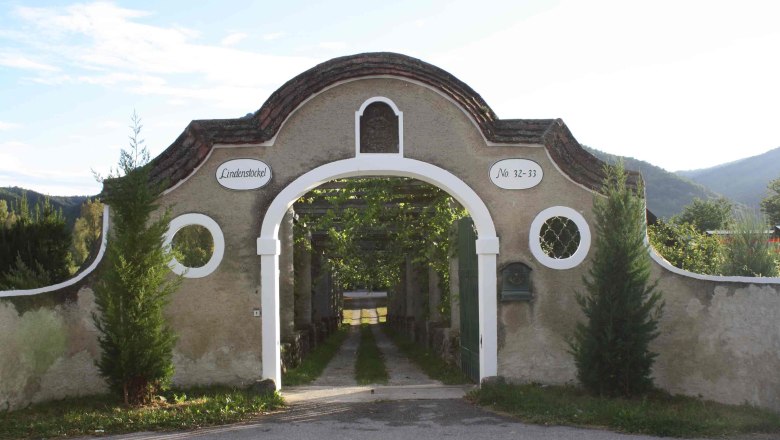 Access to the Schmidl organic winery, © Familie Schmidl Entrance gate with round arch and inscription 'Lindenstöckel', surrounded by nature.