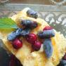 A dessert with yellow ice cream, red and blue berries, garnished with a green leaf, in a glass bowl.
