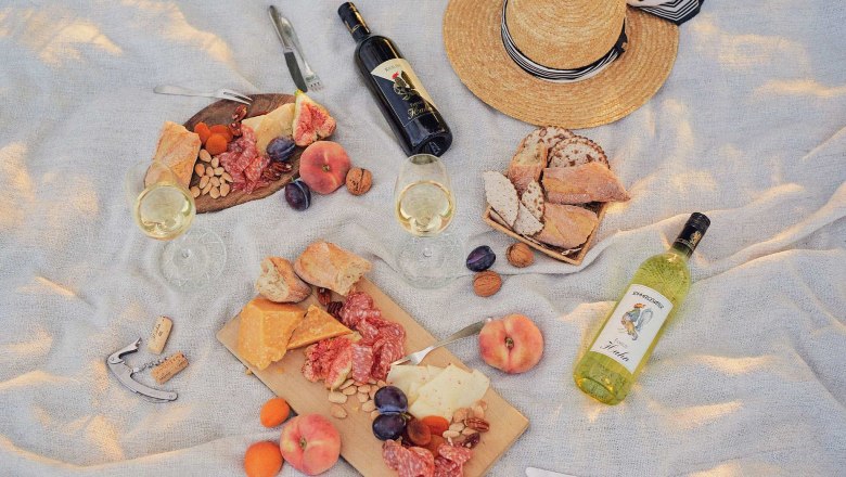 Picnic with wine, cheese, bread and fruit on a blanket.