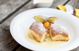 Three Buchteln with powdered sugar and physalis on vanilla sauce on a white plate.