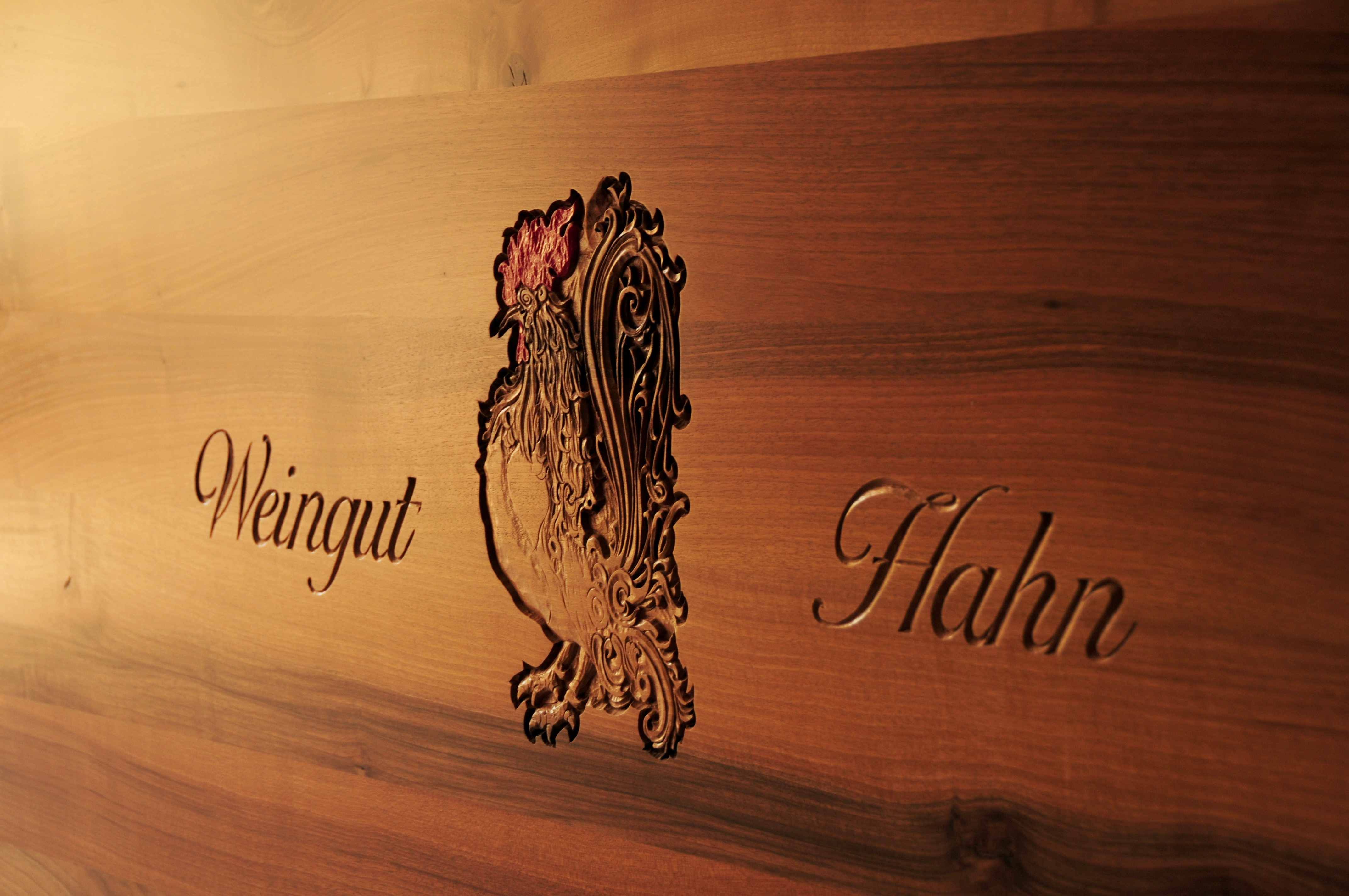 Wooden plaque with engraved rooster and 'Weingut Hahn' lettering.