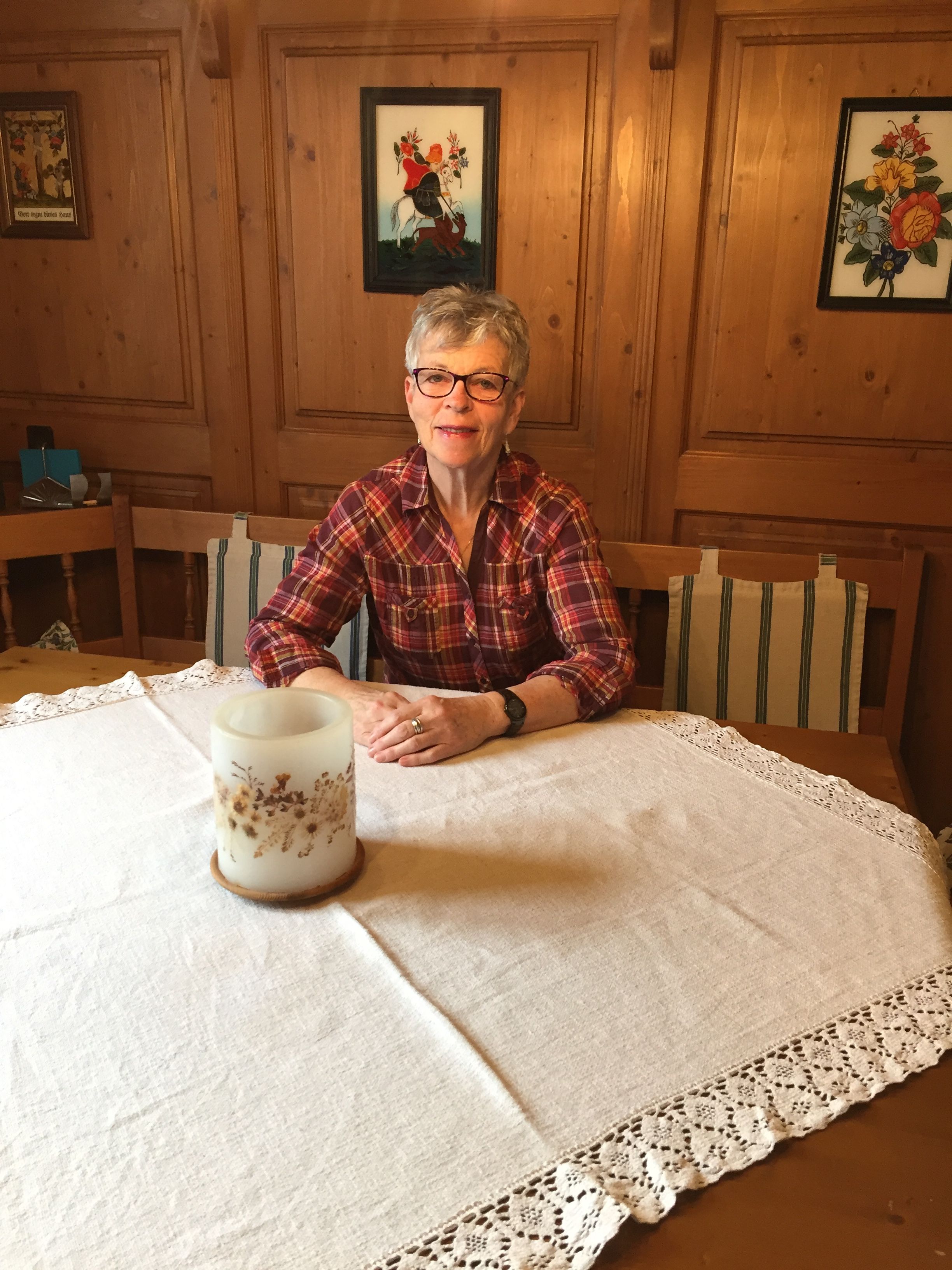 A woman sits at a table with a white tablecloth in a wood-paneled room.