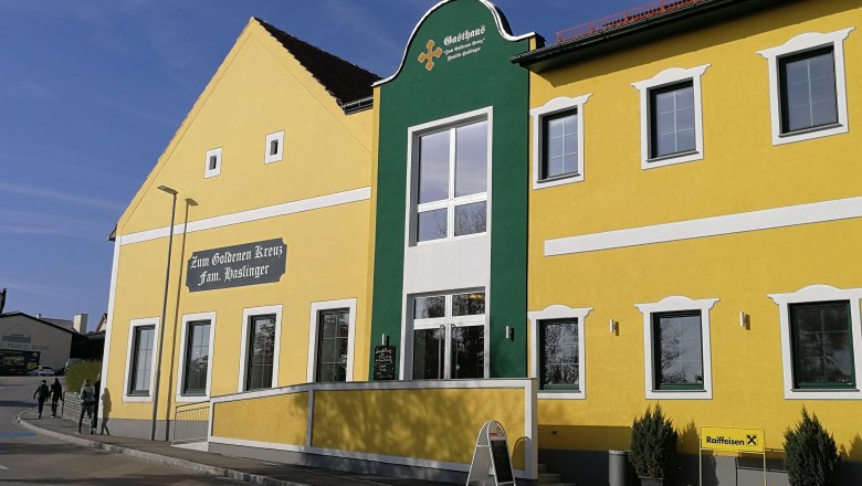 Yellow building with green façade and the inscription 'Zum Goldenen Kreuz Fam. Haslinger'.