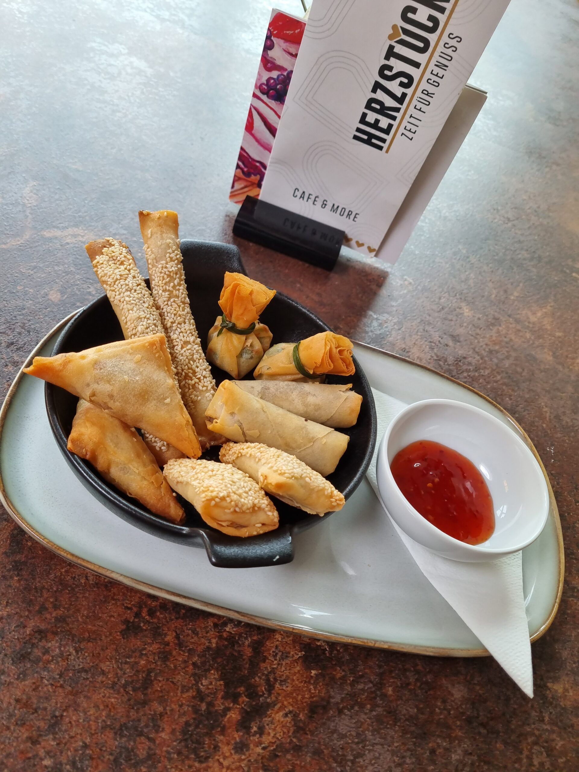 Various fried snacks on a plate with dip and café centerpiece menu in the background.