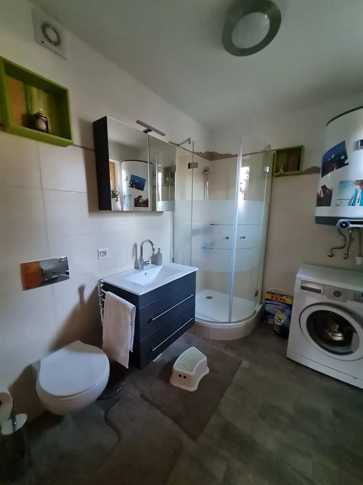 Modern bathroom with shower, washbasin, toilet and washing machine.