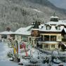 A snowy alpine-style hotel with towers and balconies, surrounded by snow-covered trees and hills.