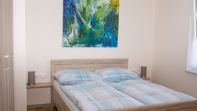 Bedroom with double bed, abstract painting on the wall and window with curtain.