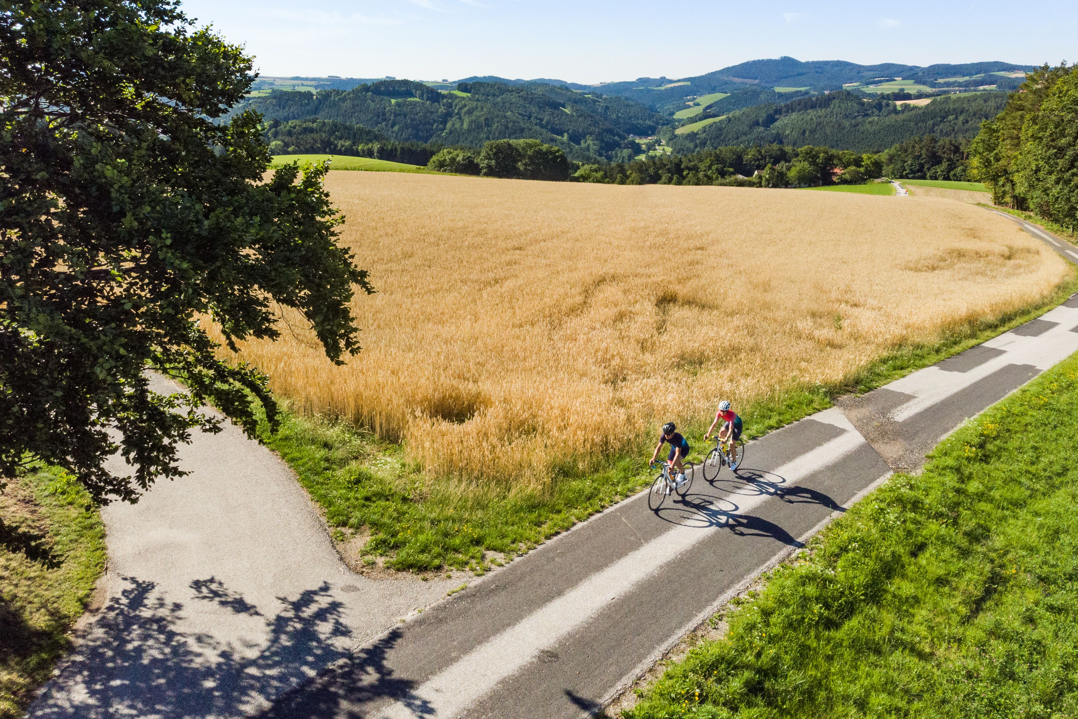 Aerial view of two people on racing bikes next to a field, hills in the background