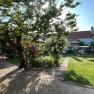 A sunny garden with table, chairs, flowers and a swinging bench.