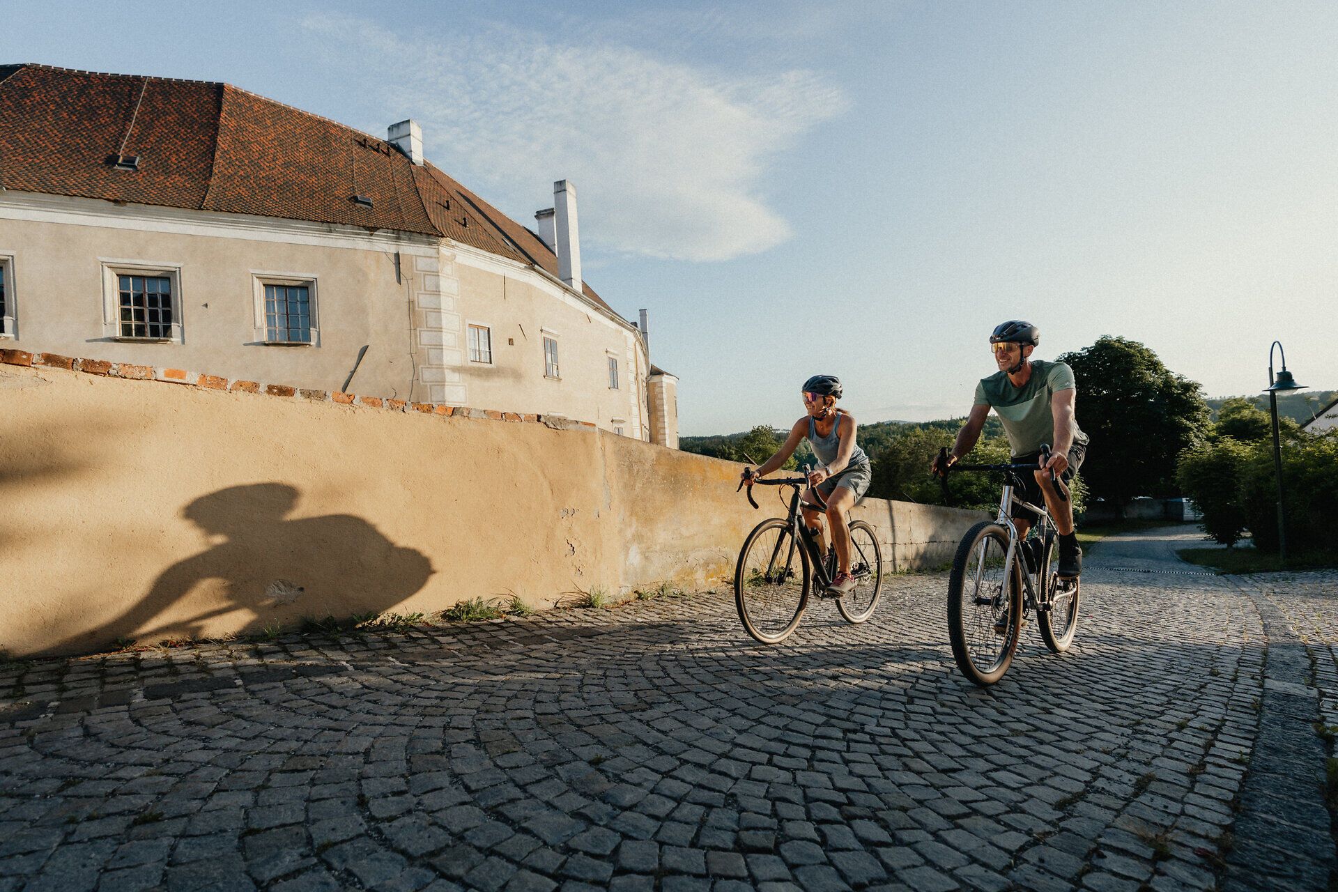 Two cyclists ride on a cobbled road along an old town wall in Drosendorf.