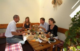 Four people sit at a table in a cozy courtyard and enjoy a meal.