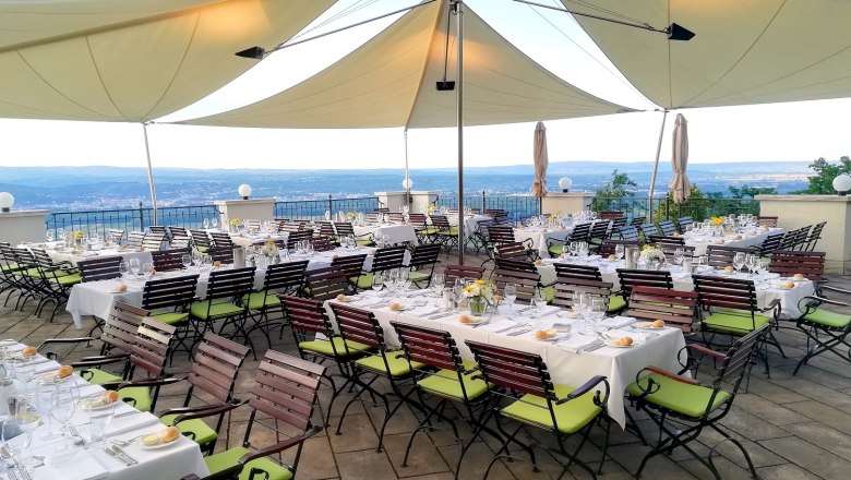 Set tables on a terrace with a view of the countryside, under large awnings.