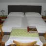 A double bed with white comforters, two bedside tables with lamps and a small table with two chairs in the foreground.
