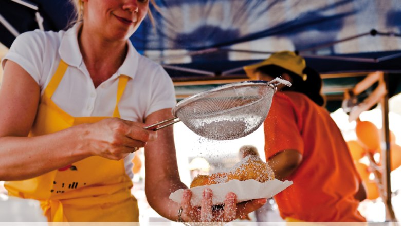 A woman dusts pastries with powdered sugar through a sieve.
