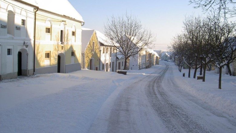 Snow-covered street with historic buildings and trees in Straning, Austria.