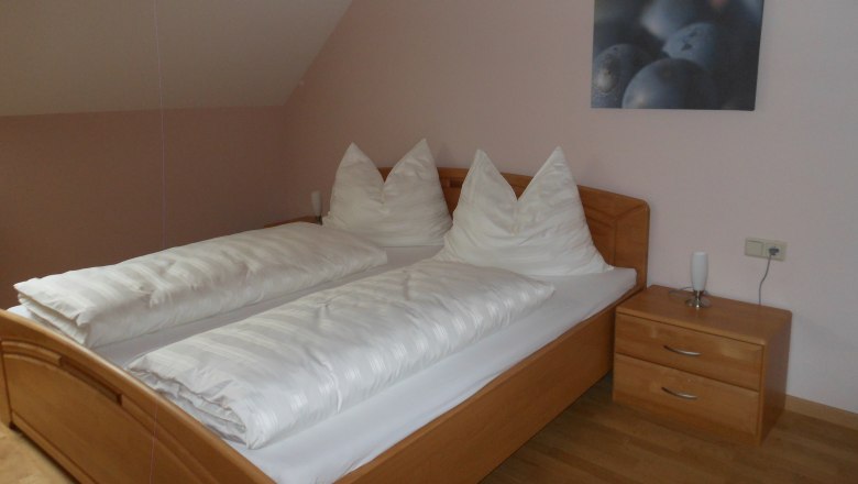 A simple guest room with a double bed, white comforters and a bedside table with lamp.