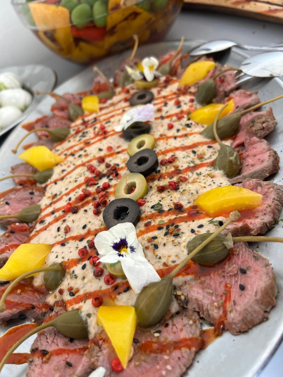 Close-up of a decorative plate of pink, finely chopped meat with capers, olives and edible flowers.