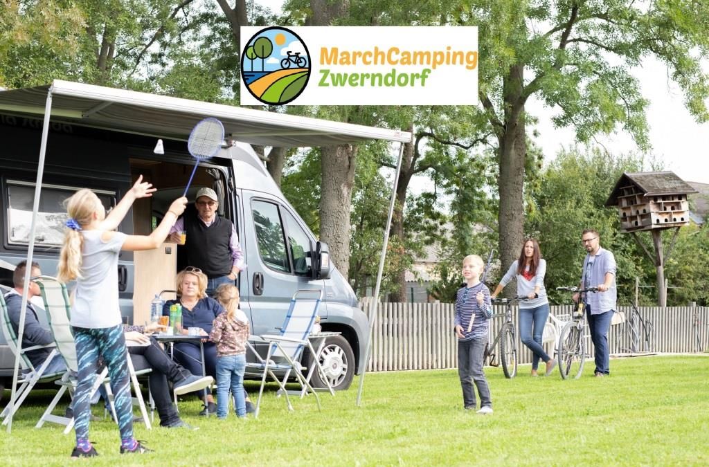 Family camping with motorhome and playing badminton on a meadow.