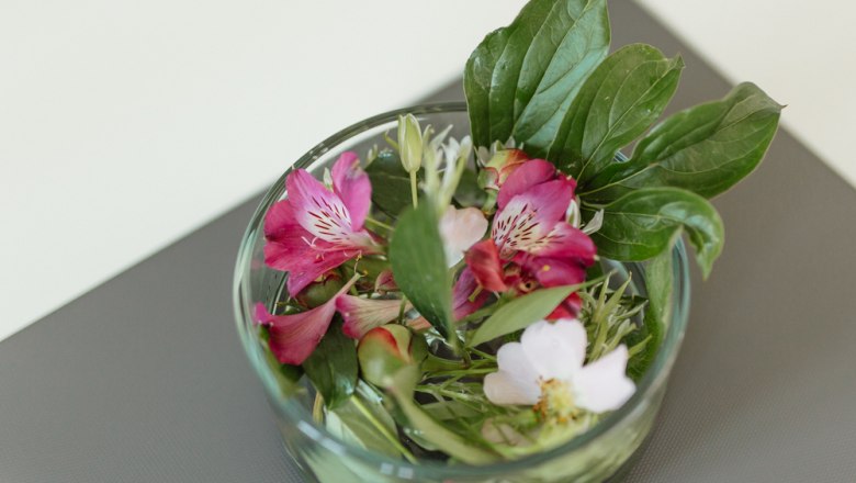 A glass jar with colorful flowers and green leaves on a table.