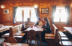 In der gemütlichen Atmosphäre einer traditionellen Hütte genießen die Gäste köstliche Speisen und die Gesellschaft von Freunden. Das warme Holzinterieur und die sanften Lichtstrahlen schaffen eine einladende Stimmung, die zum Verweilen einlädt. Hier wird der Winter in den Wiener Alpen zu einem unvergesslichen Erlebnis.