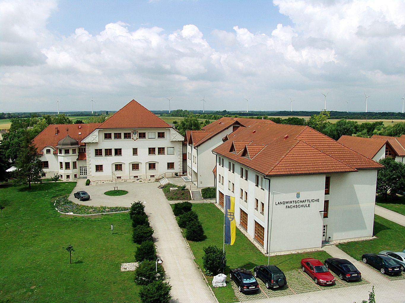 Aerial view of a school building complex with red roofs and surrounding green areas.