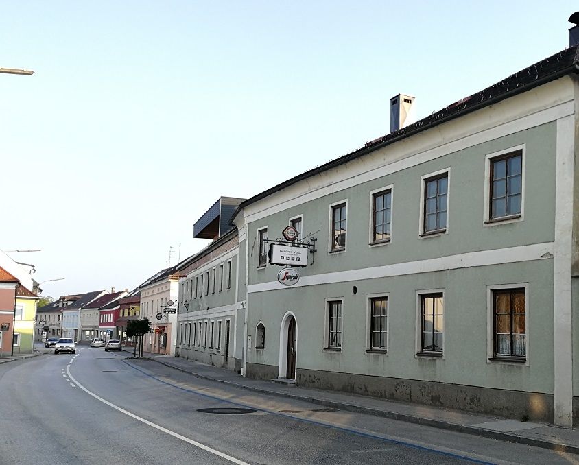 Street with Gasthof Veigl in a green building, next to it other houses.