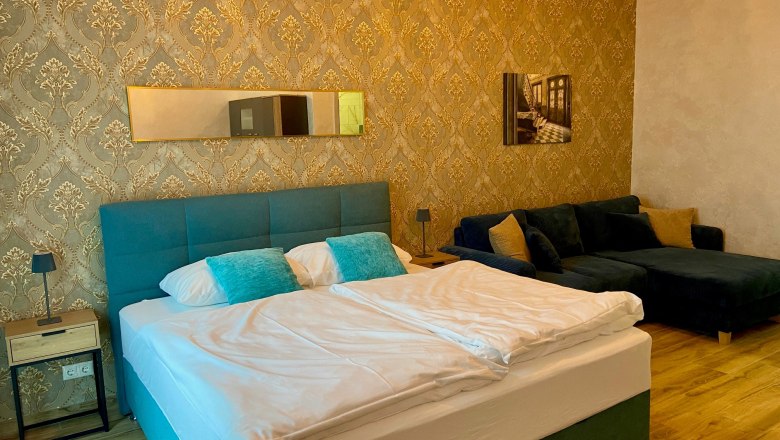 Elegant hotel room with double bed, blue couch and golden wallpaper.