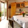 Cozy kitchen with wooden furniture, dining table and bouquet of flowers. Open balcony door with a view of the greenery.