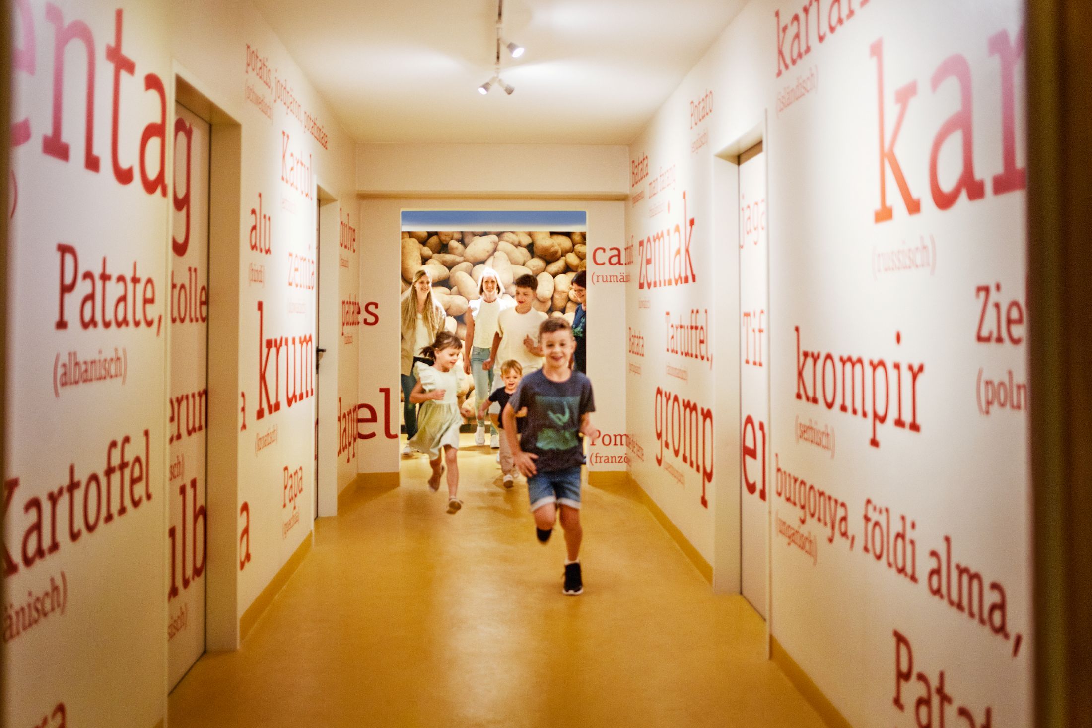 Children run through a corridor with potato words in different languages on the walls.
