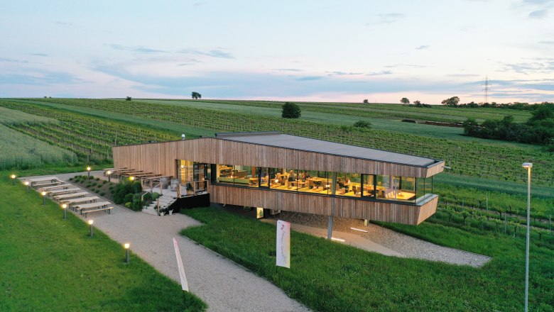 A special kind of wine tavern, © Weingarten.rocks Modern building surrounded by vineyards at sunset.