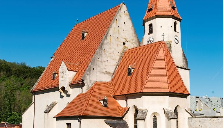 Edlitz fortified church with many side sections, red tiled roofs, a pointed tower and blue sky.