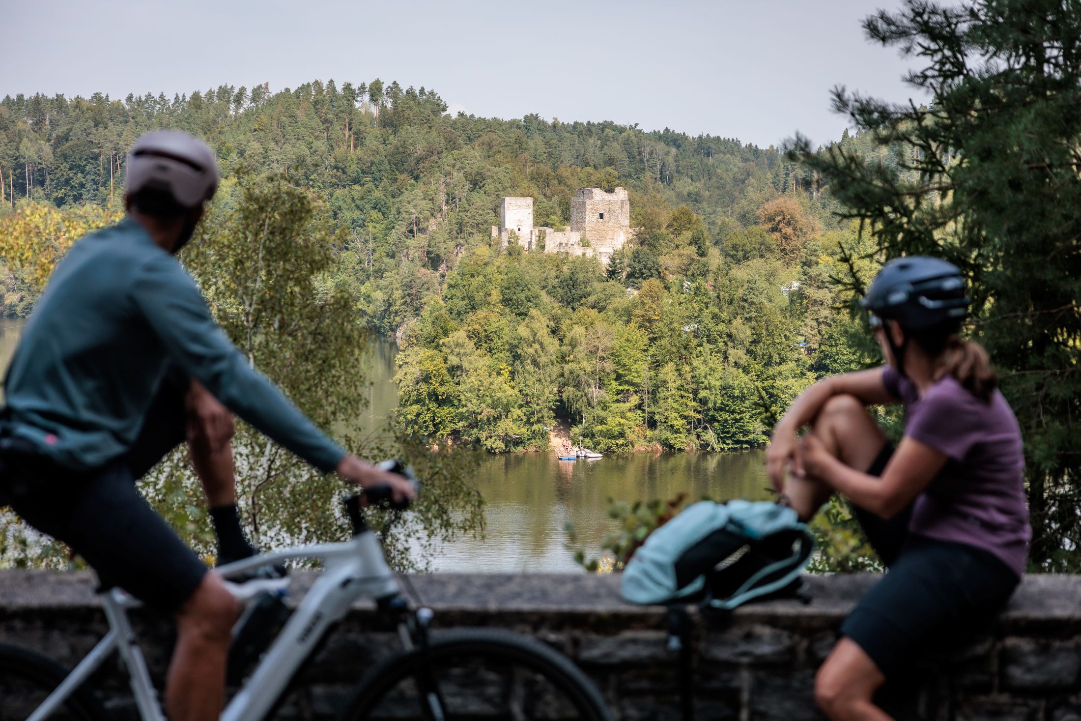 Two cyclists look at the Dobra ruins across a lake.