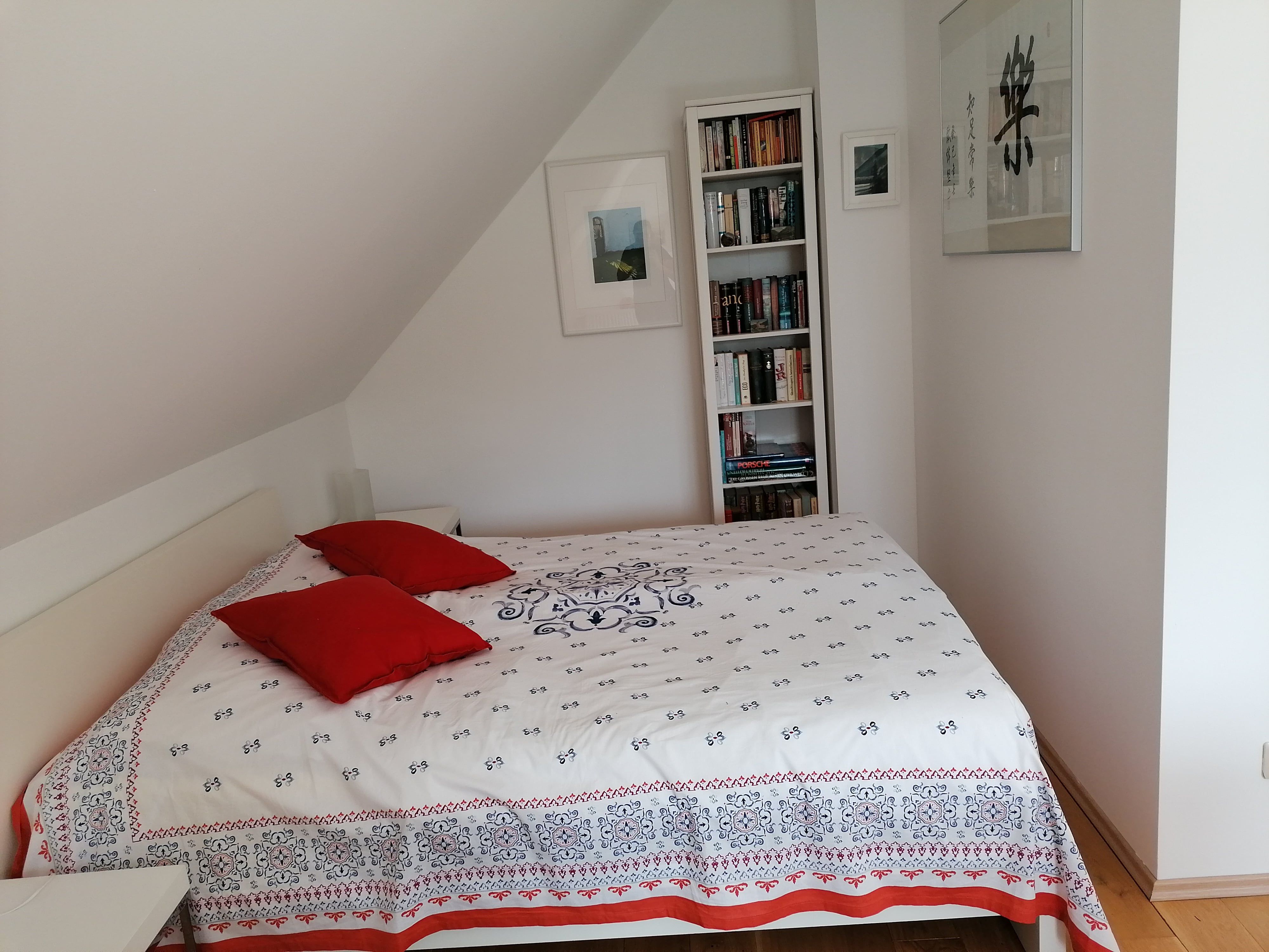 Bedroom with bed, red cushions and bookshelf.