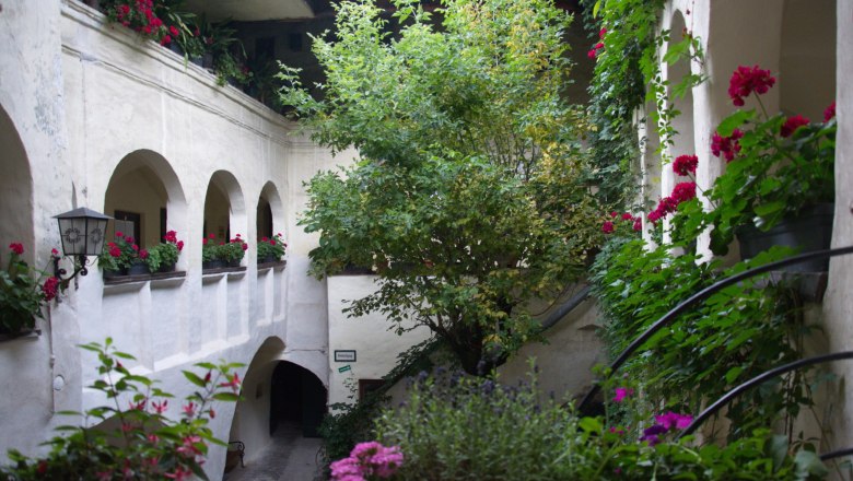 Inner courtyard, © Einzinger GmbH An inner courtyard with plants and flowers in pots, surrounded by white walls and arches.