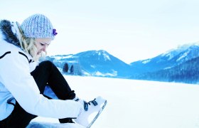 Person puts on ice skates on a snowy lake surrounded by mountains.