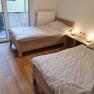 Two single beds in a bright room with wooden floor and balcony access.