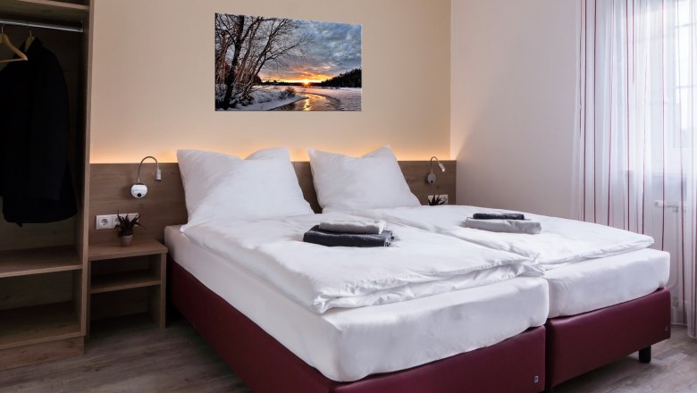 Modern double room with two single beds, picture on the wall, closet and window with curtains.