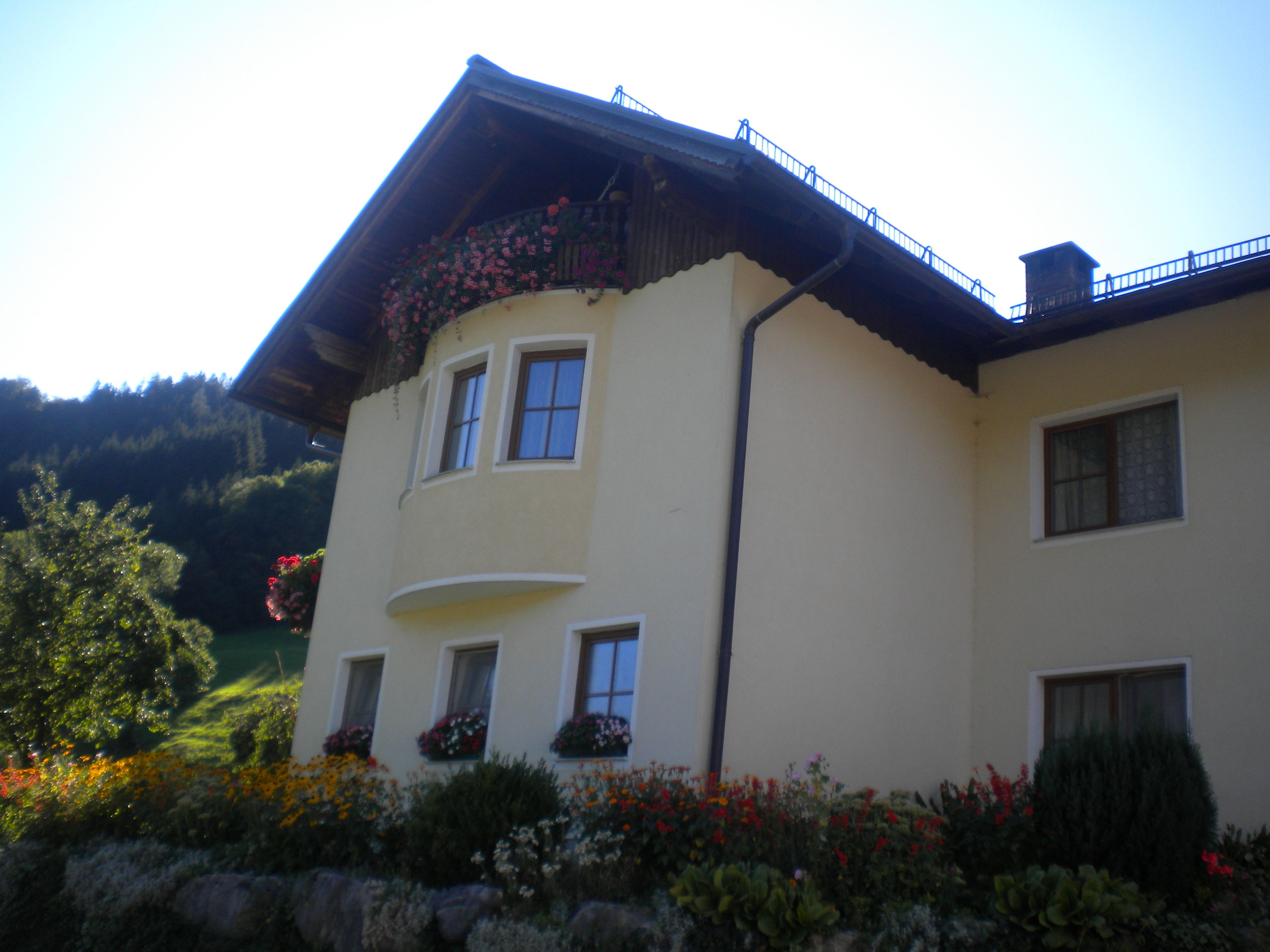 Yellow house with flowers and balcony in front of a wooded hill.