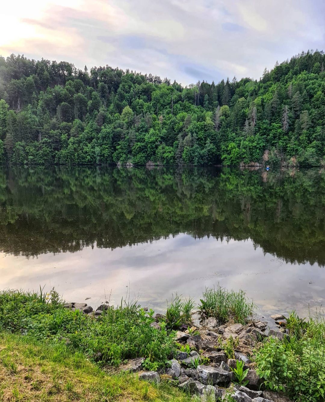 A calm lake with wooded hills in the background that are reflected in the water.
