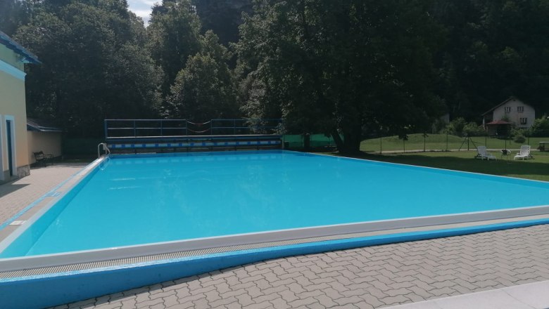 An empty outdoor swimming pool surrounded by trees and a building.