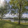 Panoramic view of a lake with trees and a bench in the foreground, sunny sky.