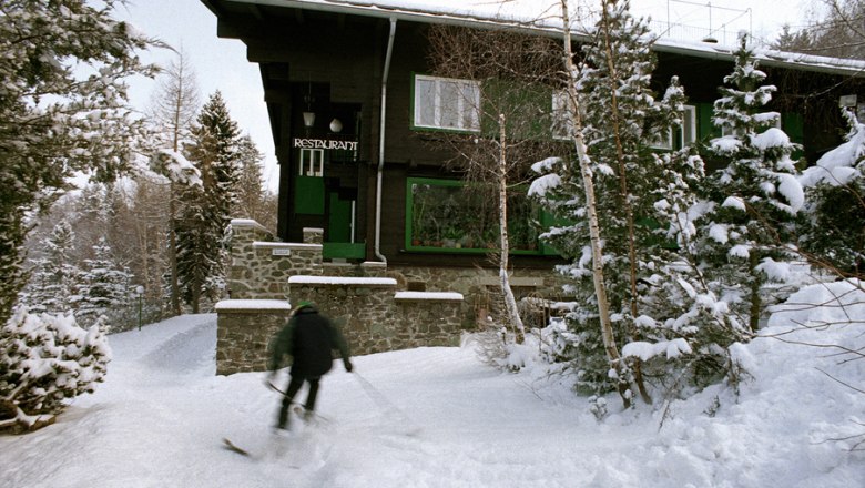 A skier passes a snow-covered building that serves as a restaurant.