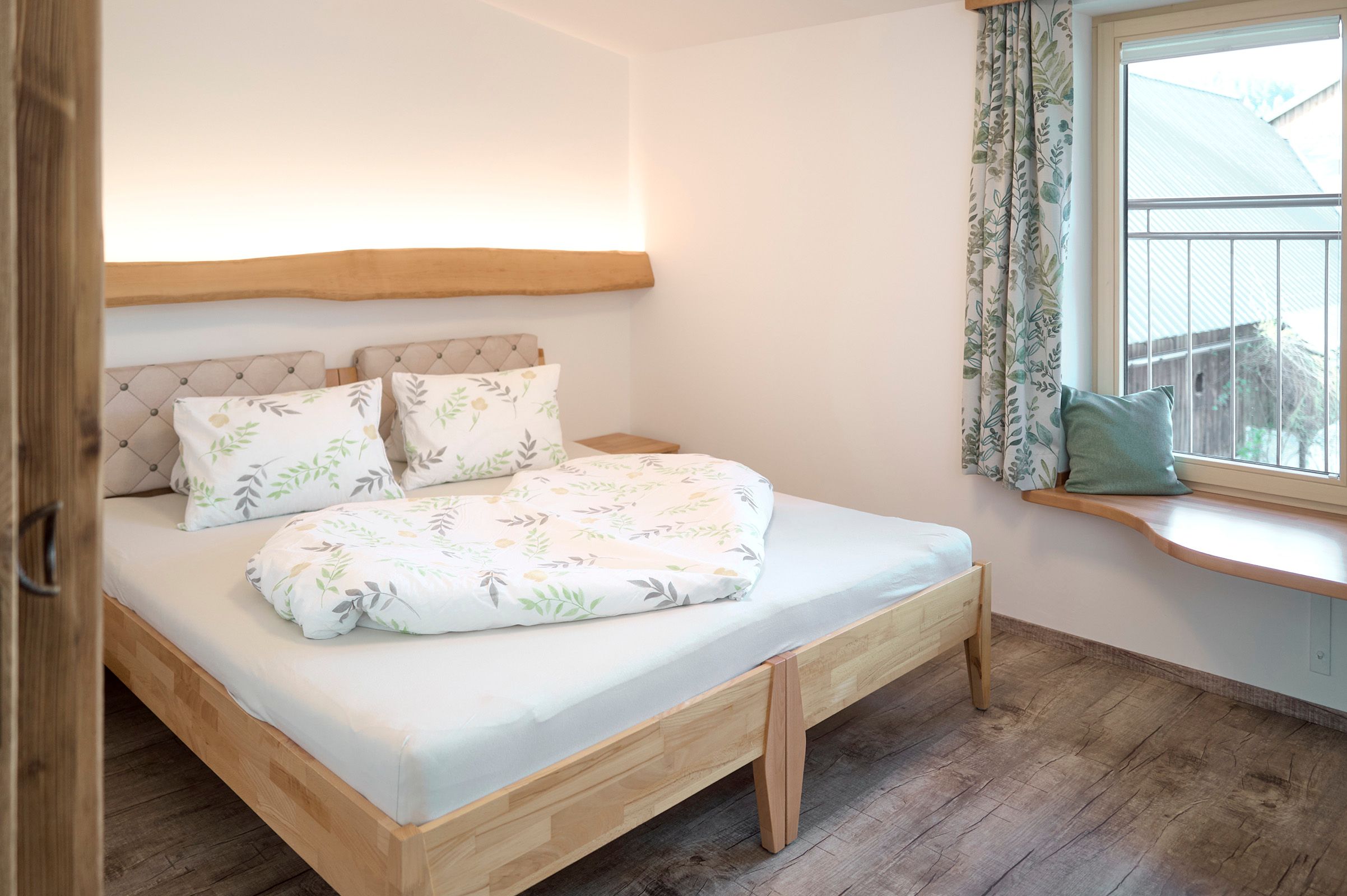 Cozy bedroom with double bed, wooden floor and window with curtains.