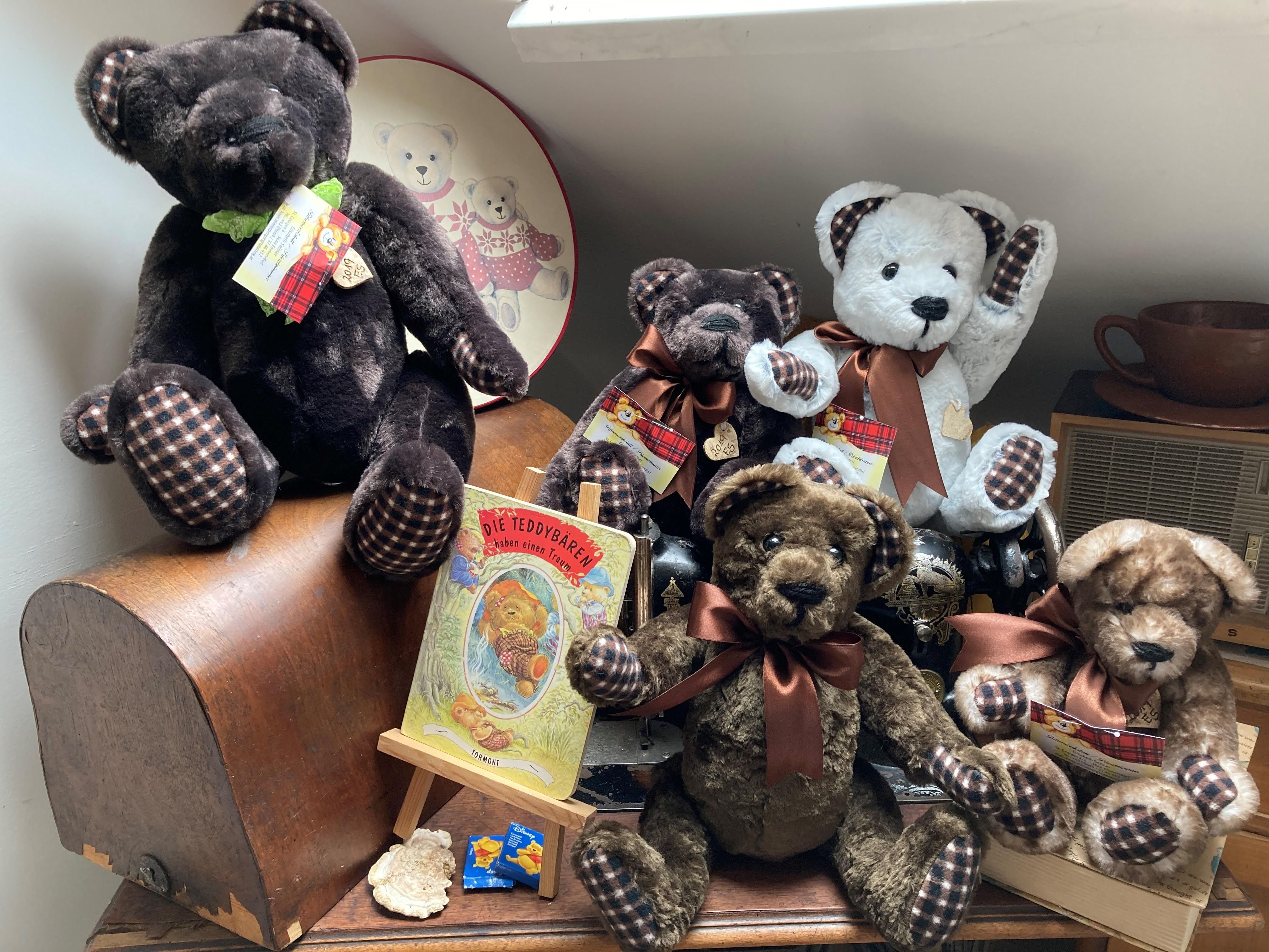 A collection of teddy bears on a table, surrounded by decorations and a book about teddy bears.