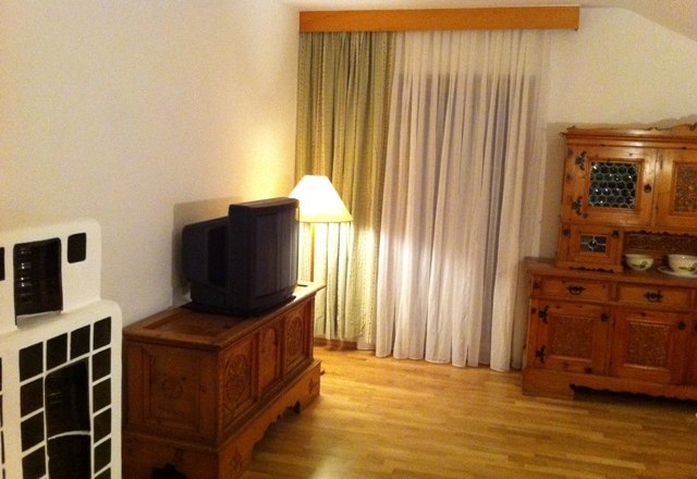 A living room with wooden furniture, an old television, a floor lamp and curtains.