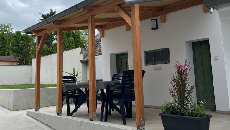 Covered terrace with table and chairs, surrounded by plants.