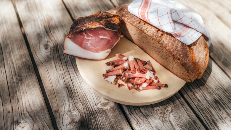 A wooden board with bread, bacon and strips of bacon on a wooden table.