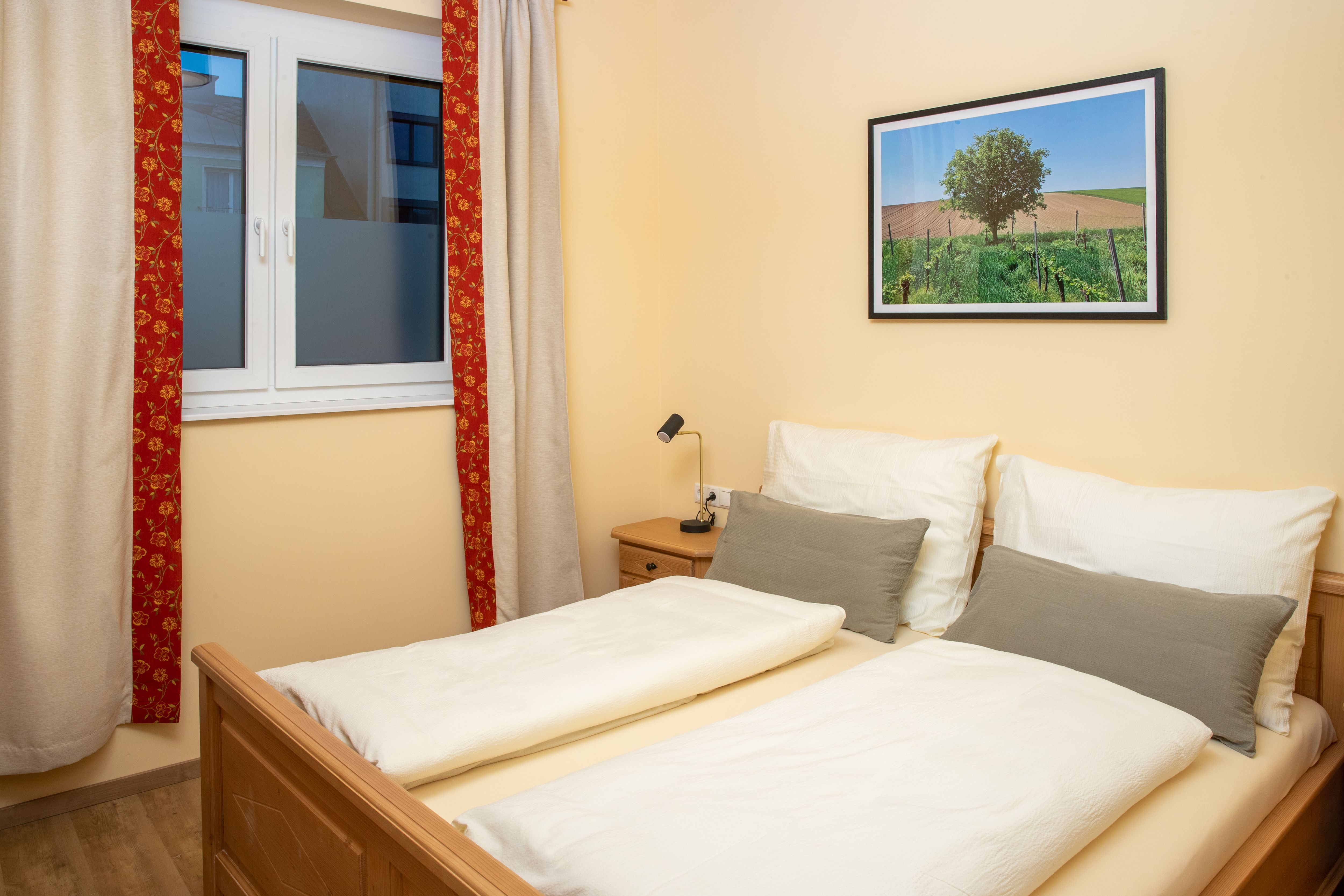 A cozy double room with a double bed, a window with curtains and a landscape painting on the wall.