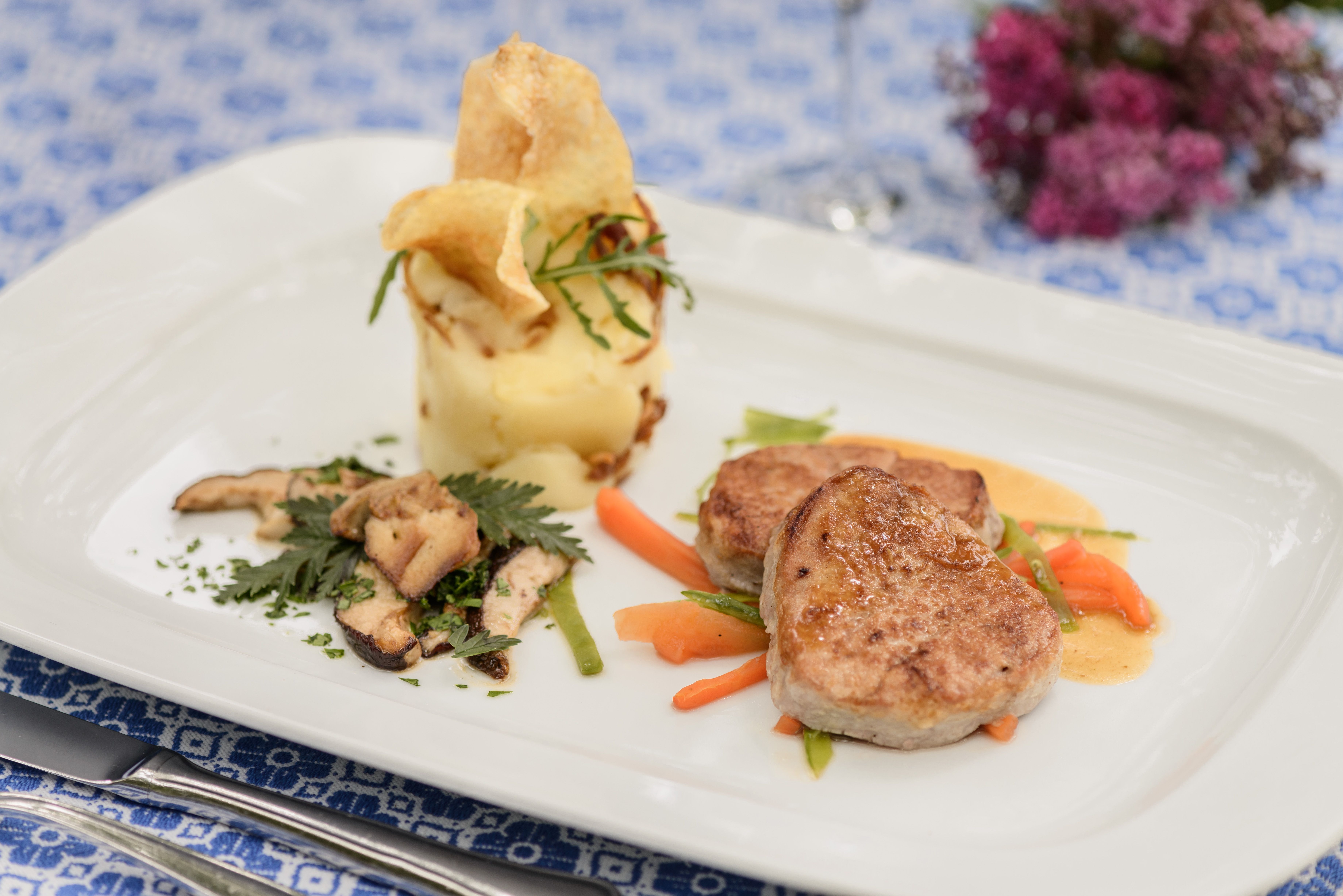 Gourmet dish with meat, mashed potatoes and vegetables on a white plate.